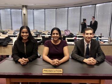 Three Mock Trial Competitors sitting at a desk in a courtroom. 